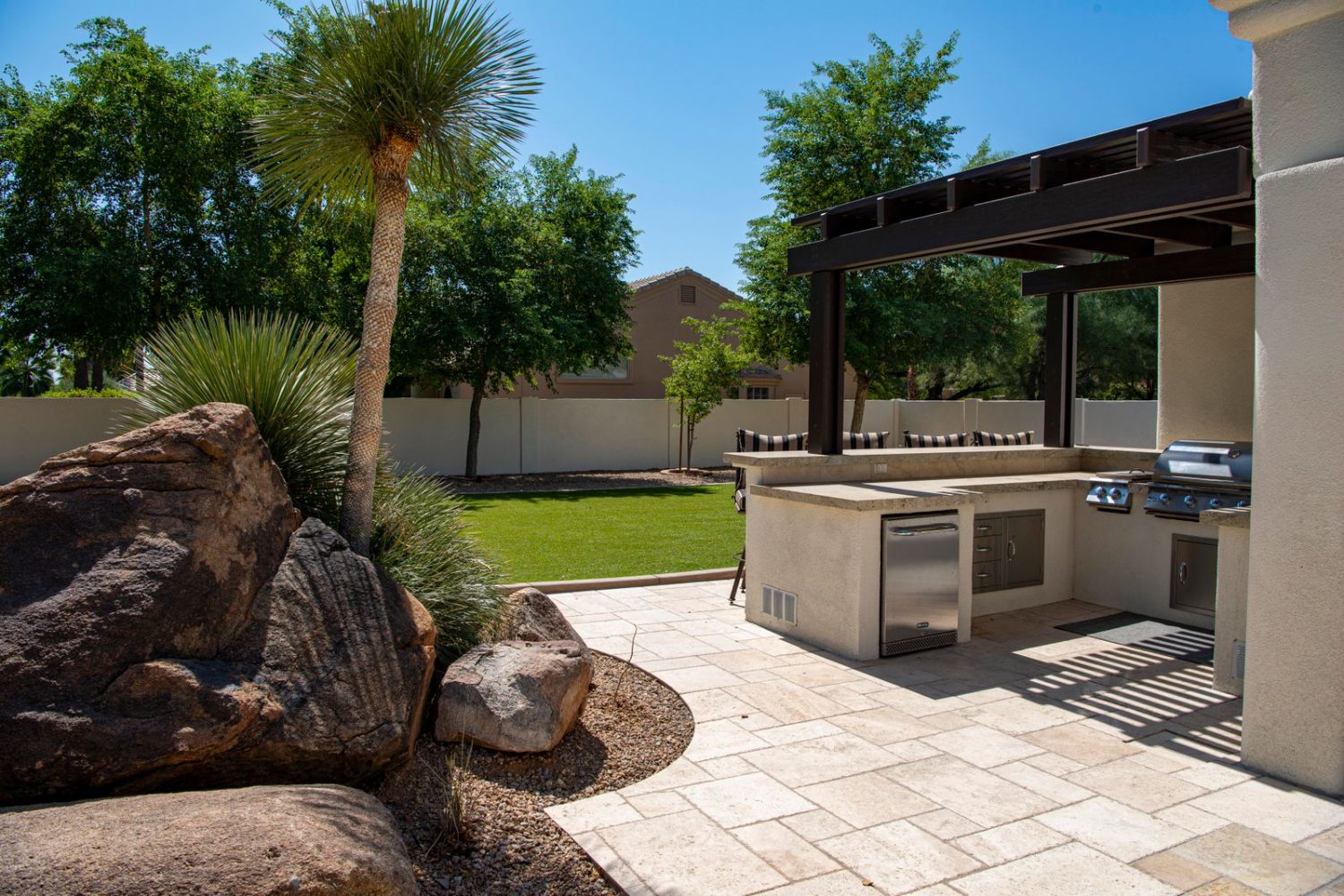 A covered outdoor kitchen and pergola on a desert paver patio.