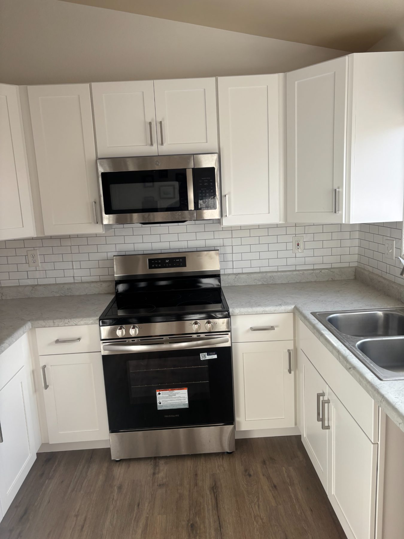 White shaker cabinets and a stone-look countertop beside a stainless range, by Inferno Construction.