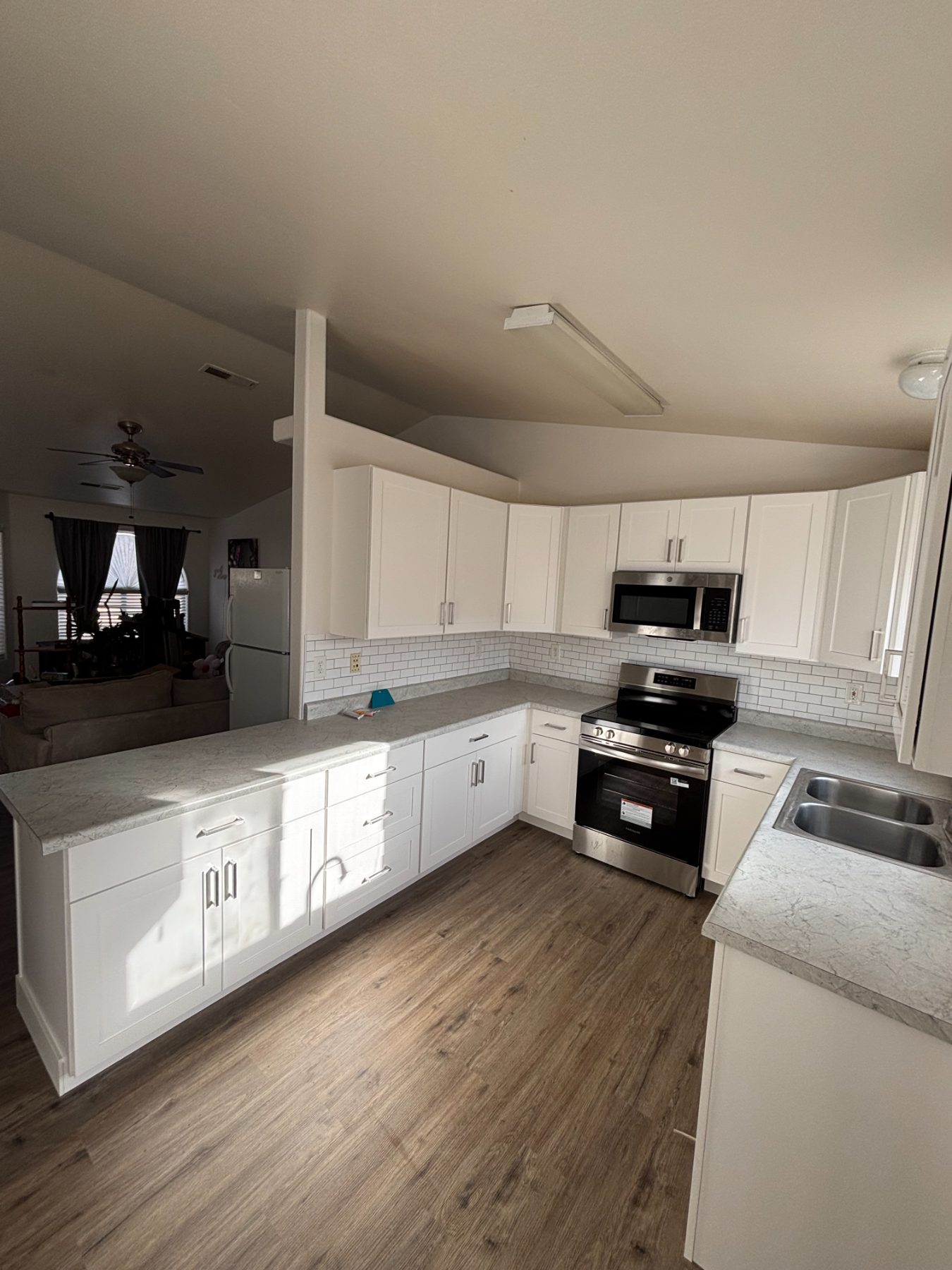 A finished Inferno kitchen with white shaker cabinets, stone-look countertops, a subway tile backsplash, and wood-look vinyl plank flooring.